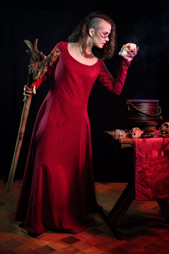 Costume medieval fantasy de sorcière rouge avec des cranes et un chaudron